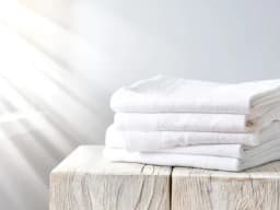 Zusammengelegte, strahlend weiße Wäsche liegt sauber auf einem Holztisch in hellem Sonnenlicht.